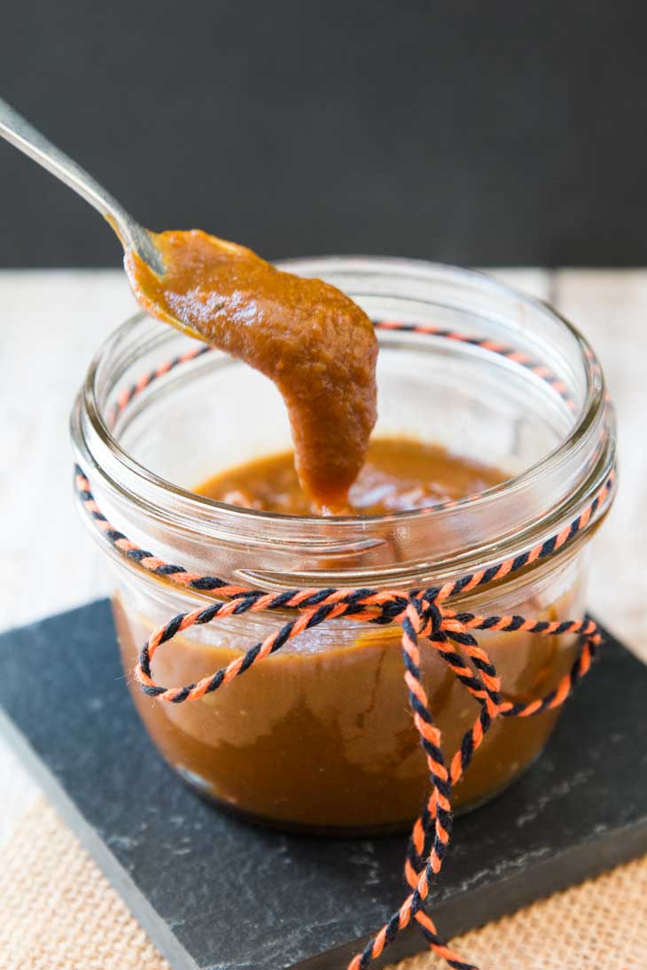 A photograph of a jar full of vegan pumpkin butter recipe. There's a spoon filled with the butter scooped up from the jar. 