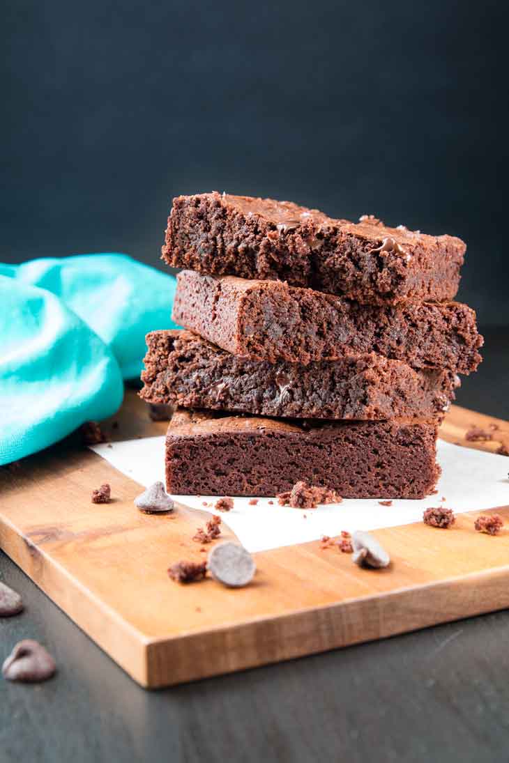 A stack of richa's vegan brownie recipe sitting on parchment paper and a wooden board. 