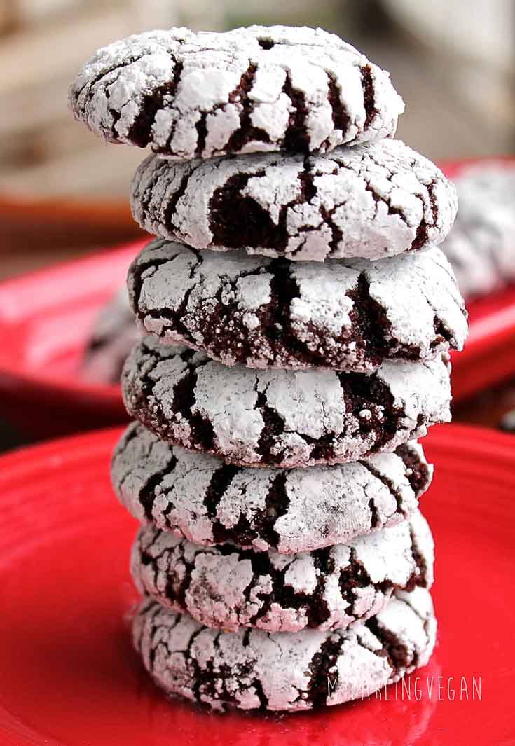 A stack of chocolate crinkle holiday vegan cookies sitting on a red plate.