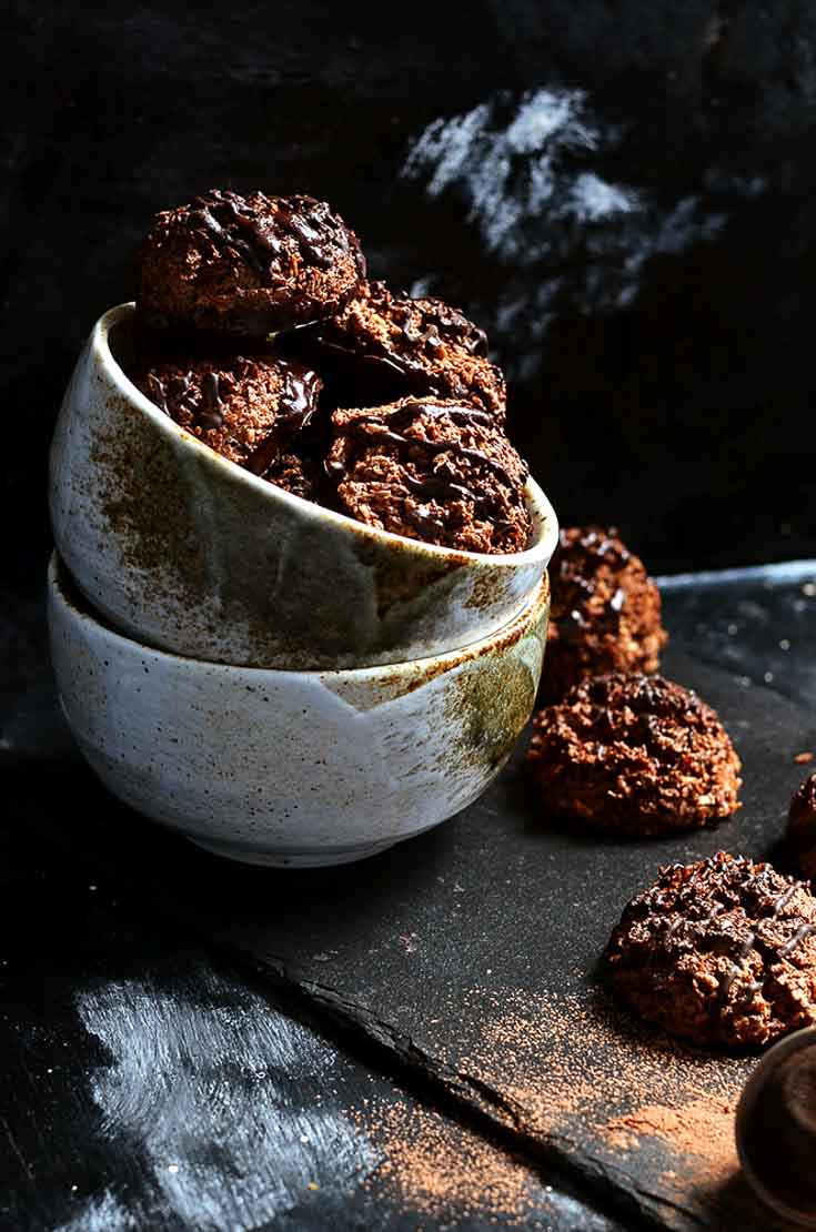 Cocoa Coconut Macaroons sitting in a double stacked bowl. There are some cookies off to the side with cocoa powder dusted on the surface. 
