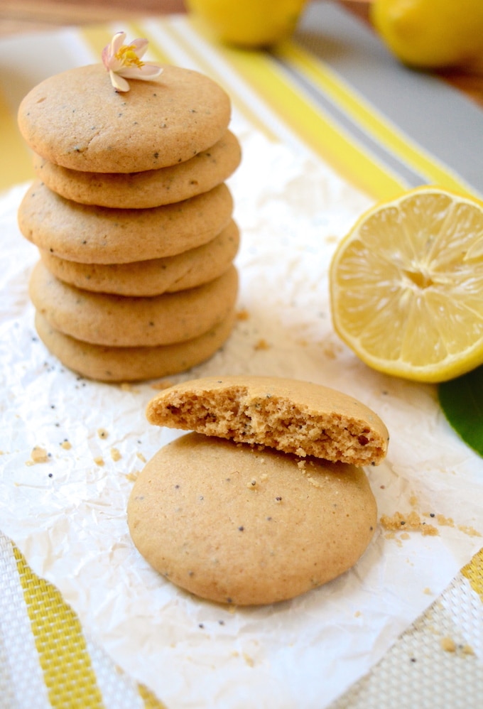 A stack of soft lemon cookies sitting on parchment paper. Another cookie is half eaten sitting in front with a lemon off to the side. 