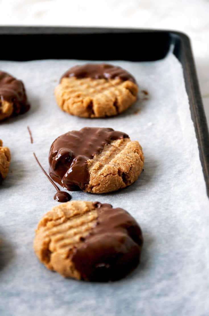 3 peanut butter cookies dipped in dark chocolate, sitting on a baking sheet. 