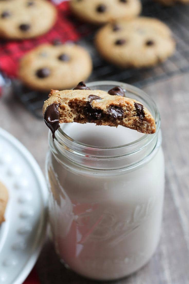 A gluten-free vegan chocolate chip cookie, half eaten, sitting on a mason jar filled with milk. 