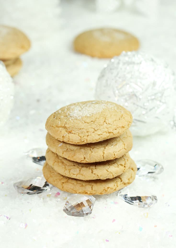 A stack of sugar cookies sitting on a white shiny sheet with gems around the outside.