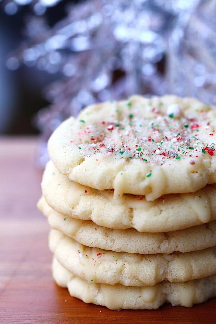 Stack of white peppermint cookies sitting on a wooden table with crushed candy canes. 