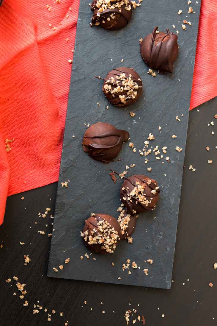 An overhead photograph of vegan pumpkin spice dark chocolate truffles sitting on a black board and red kitchen napkin.