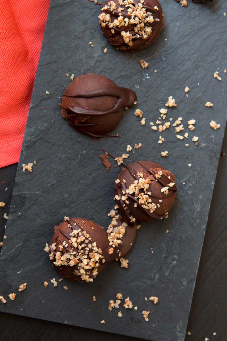 An overhead close-up photograph of pumpkin spice dark chocolate truffles sprinkled with crushed pecans. 