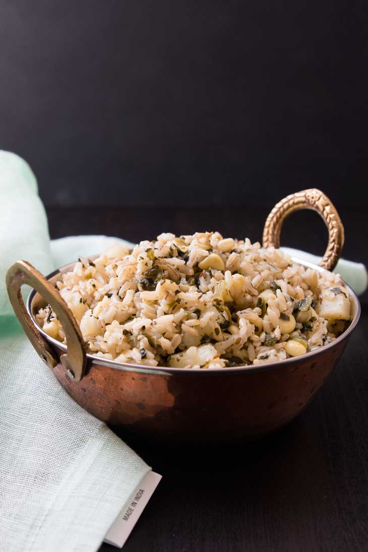 A side view of vegetable pulau rice recipe served in a copper bowl with a light green napkin sitting on the side. 