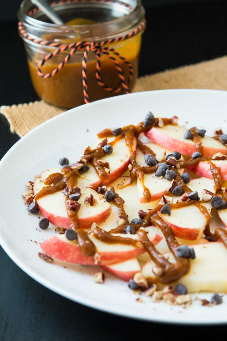 Side photograph of vegan dessert apple nachos topped with pumpkin butter, chocolate chips, and pecans.