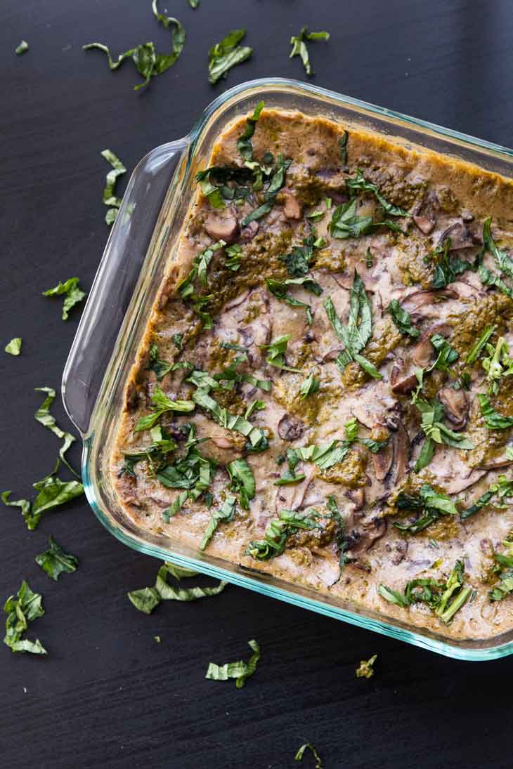 An overhead photograph of cooked vegan mushroom spinach lasagna in a glass tray with fresh basil as garnish. 