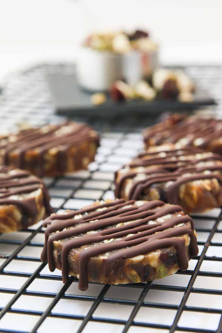 Sixth best vegan meal on VG in 2017. Side photograph of no-bake date nut cookies drizzled with melted chocolate. They are sitting on a black cooling rack. 