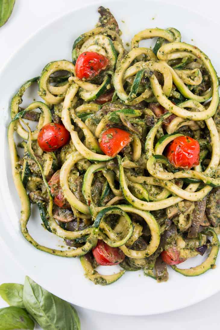 Fourth best vegan meal on VG in 2017. Overhead photograph of spiralized zucchini noodles with pesto and cherry tomatoes plated on a round white plate.