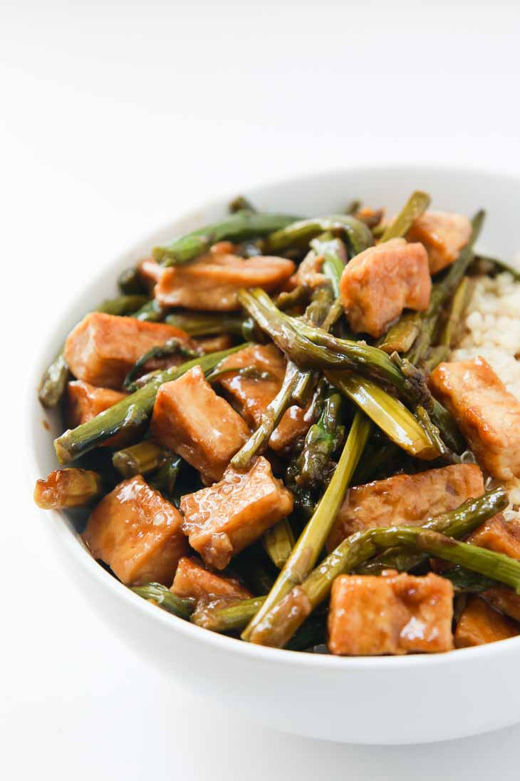 Eighth best vegan meal on VG in 2017. Side photograph of Teriyaki tofu with asparagus and cooked brown rice served in a white bowl. 