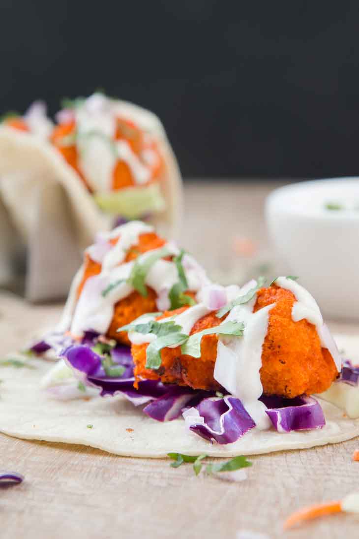 Third best vegan meal on VG in 2017. Vegan Buffalo Cauliflower Tacos with slaw and topped with ranch, sitting on a wooden board. 