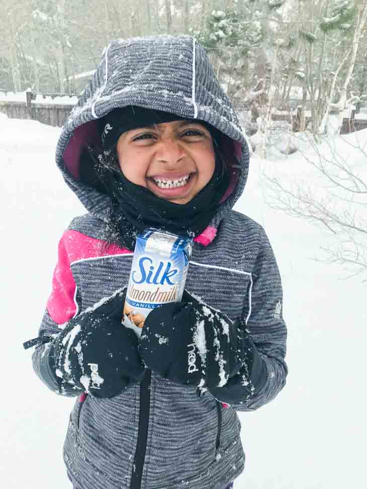 A child holding silk almondmilk single serving in the snow.