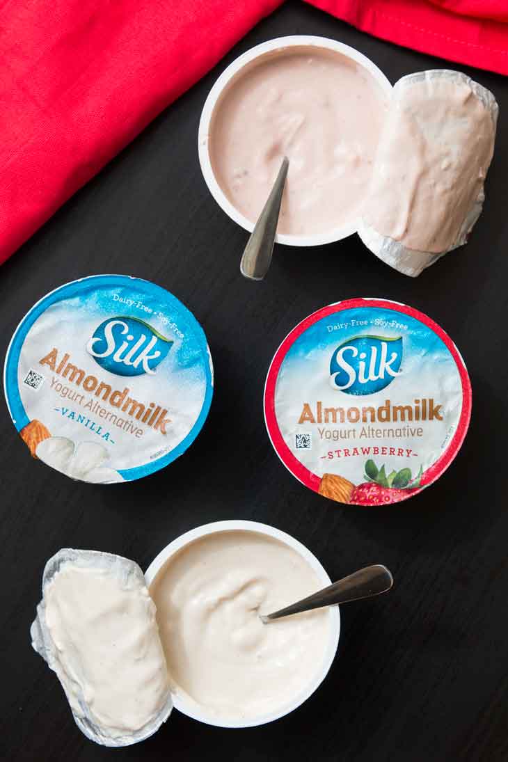 An overhead photograph of 4 single-serving SILK almondmilk yogurt . Two of the servings are open with spoons inside.