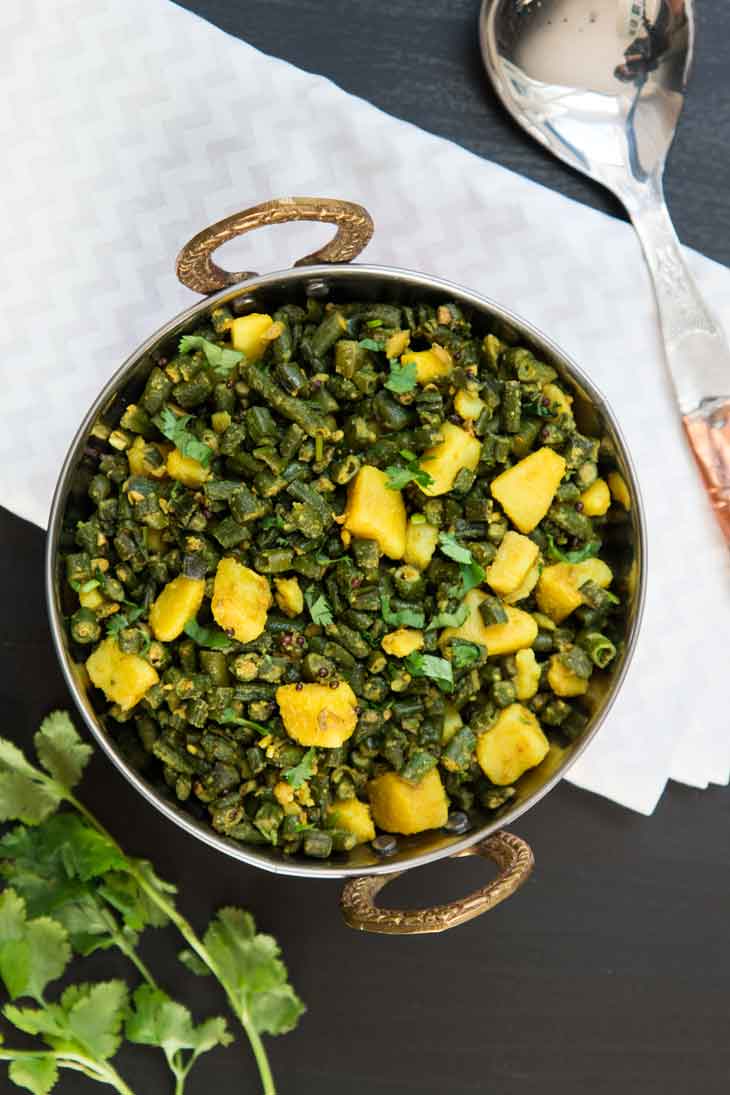 Overhead photograph of indian green bean curry with potatoes served in a copper bowl, with cilantro as garnish.