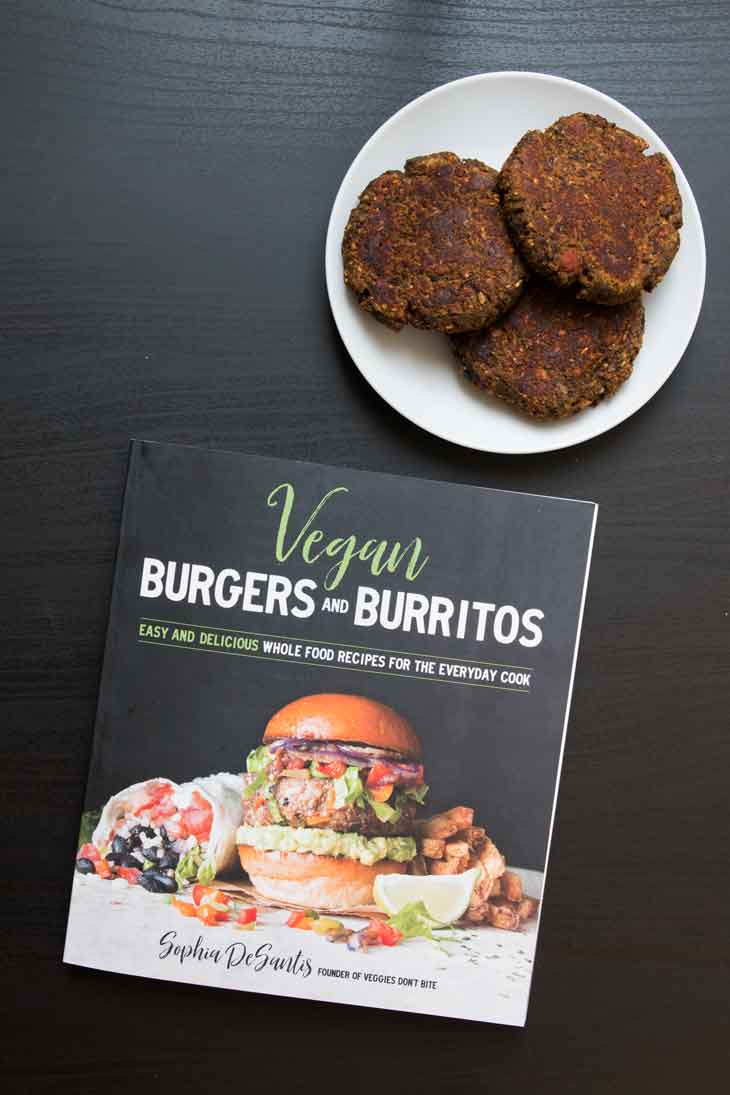 An overhead photograph of the vegan burgers & burritos cookbook. There's a side plate with patties of a vegan burger recipe out of the cookbook. 