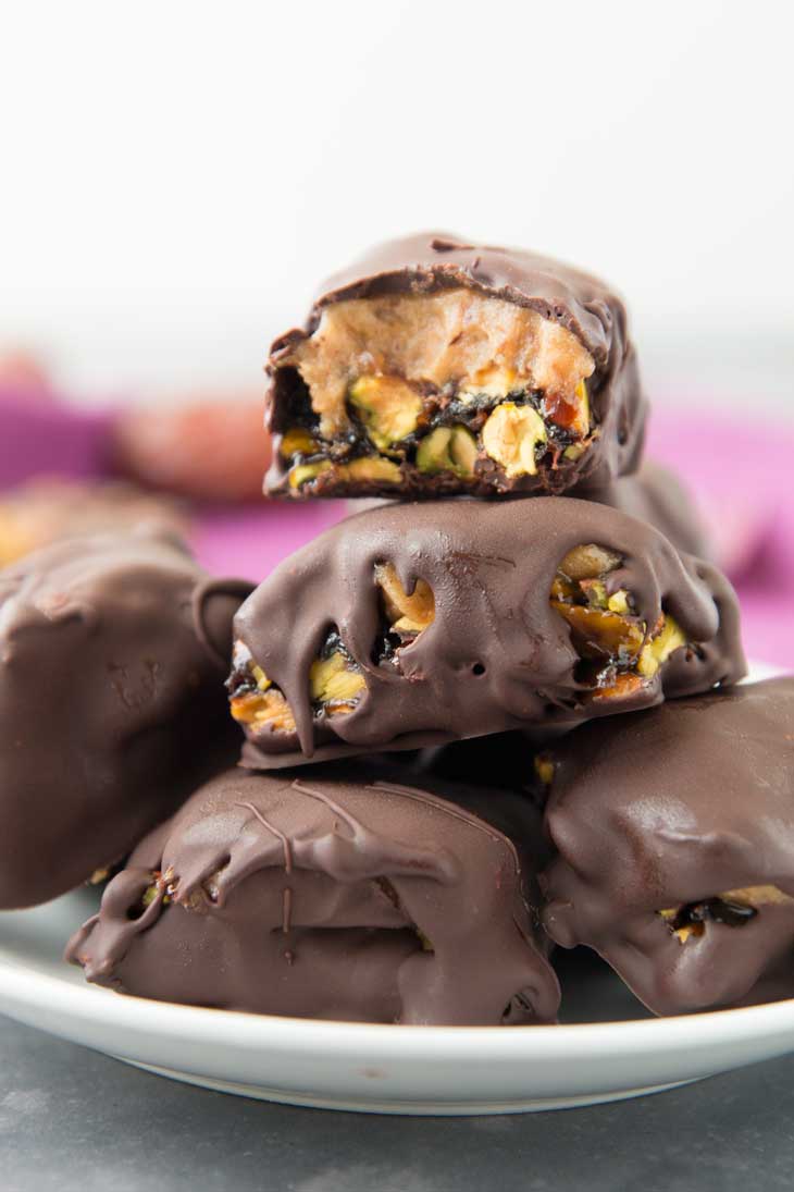 Stacked vegan chocolate bars with salted caramel and pistachio bites, covered in dark chocolate. 