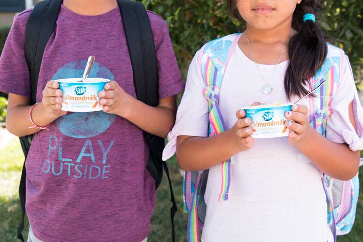 A front photograph of two kids enjoying vegan healthy yogurt cups.