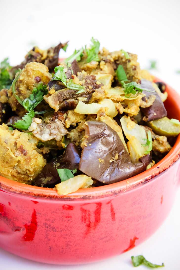 A close up of Indian spiced baked eggplant and potatoes in a red bowl