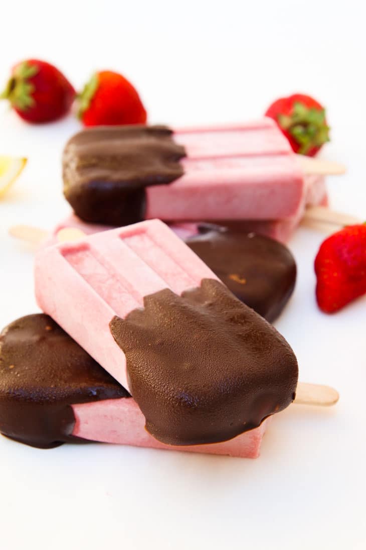 A close up of strawberry Popsicles half covered with chocolate