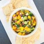 A mango and kiwi fruit salsa in a white bowl with tortillas chips