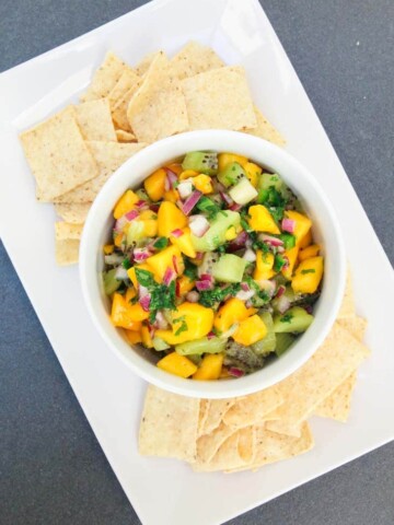 A mango and kiwi fruit salsa in a white bowl with tortillas chips