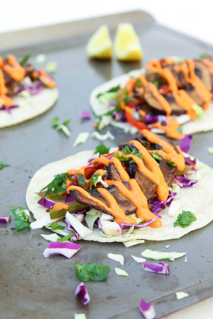 A close up of mushroom tacos with red cabbage and spicy hot sauce