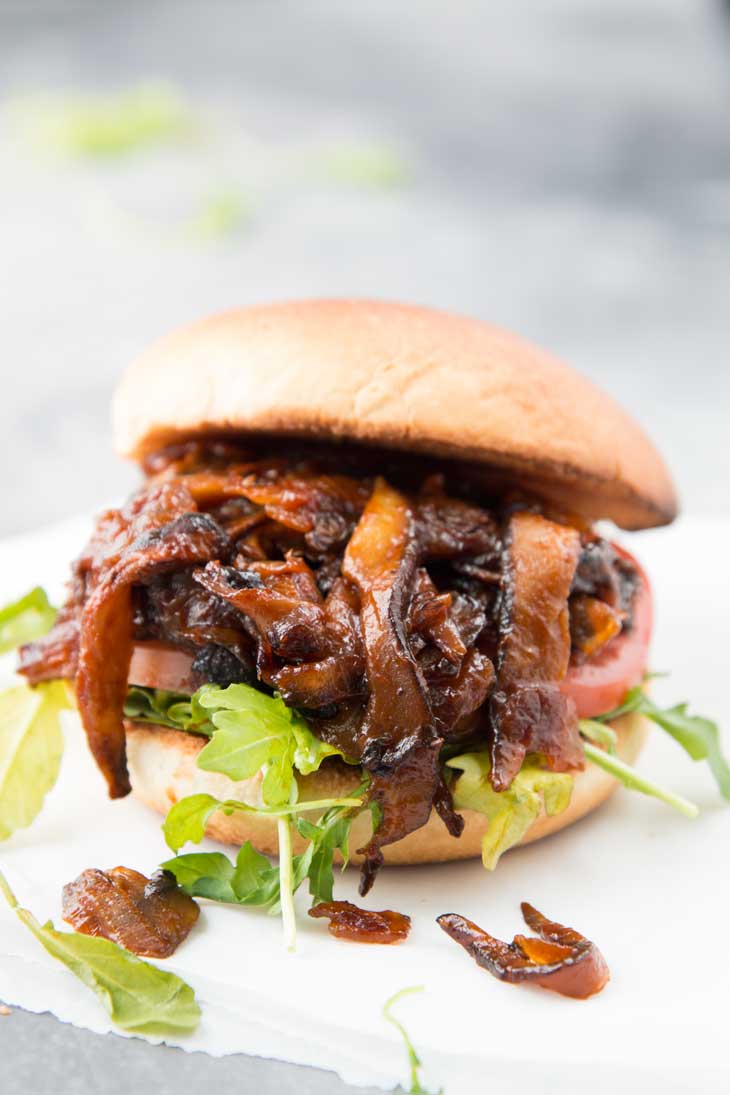 Side photograph of pulled shiitake mushroom bbq sandwich with arugula and a toasted bun.