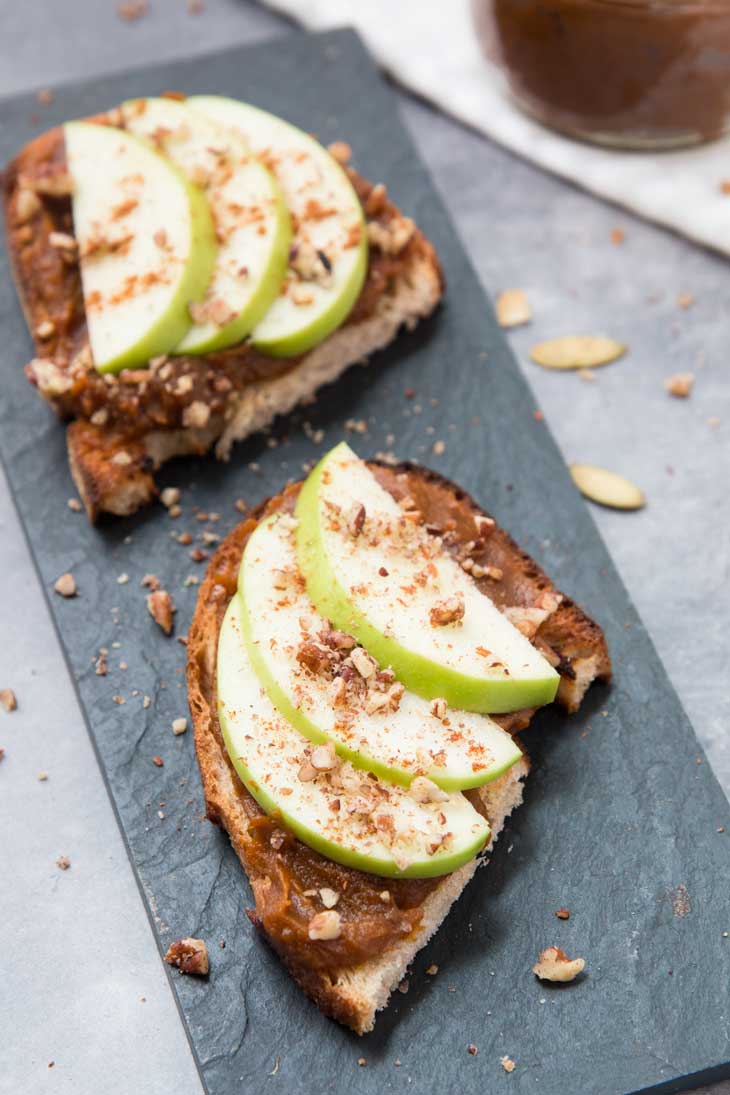 Vegan pumpkin butter toast, topped with apples & pecans! There are two pieces sitting on a black board.