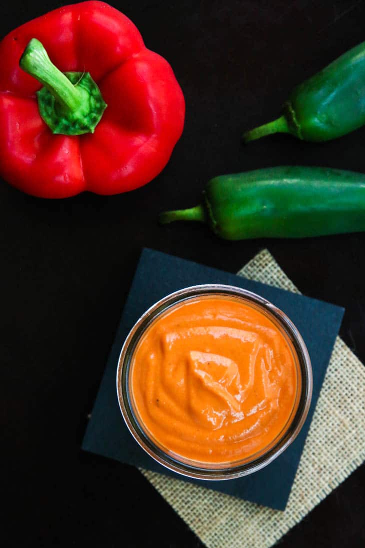 An overhead shot of roasted red pepper sauce in a jar on a black surface