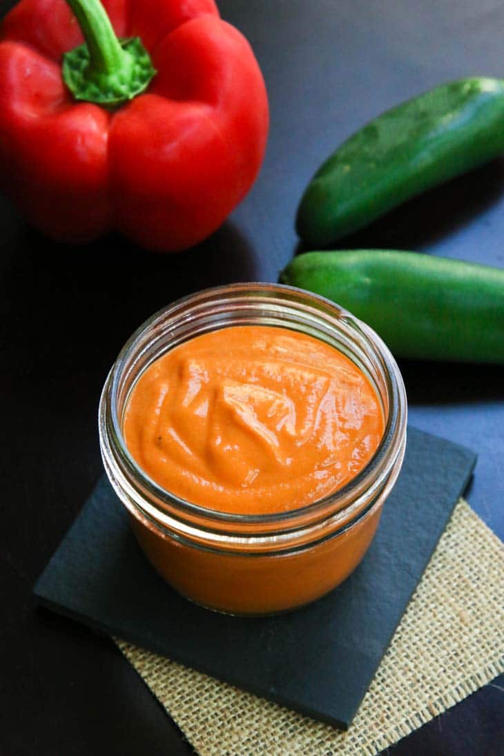 Roasted red pepper sauce in a jar with a bell pepper and chillies in the background