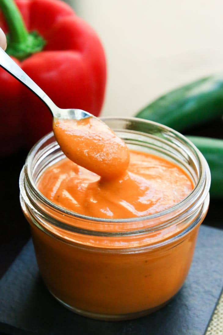 A spoon scooping up some red pepper sauce from a glass jar