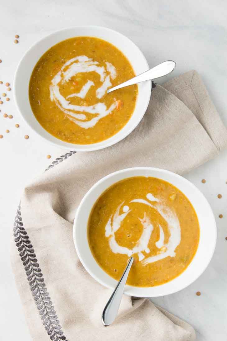 Fotografía de arriba de dos cuencos blancos llenos de sopa de lentejas vegana! Hay lentejas esparcidas por los lados.