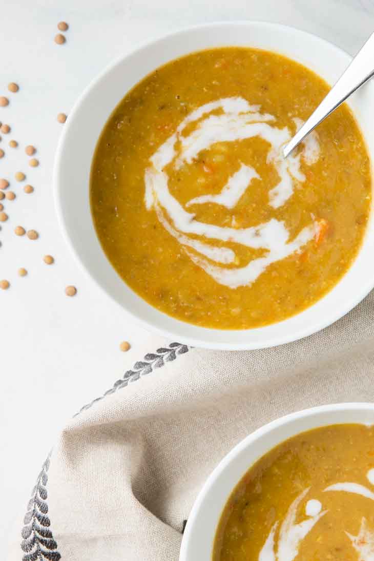 Overhead closeup of vegan lentil soup in a white bowl with uncassed lentils scattered in the background.