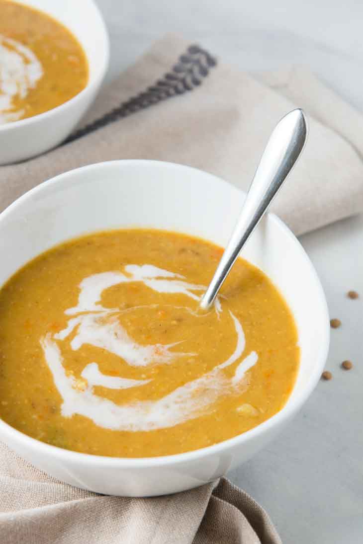 a closeup side photograph of vegan lentil soup in a white bowl, with coconut milk drizzle swirled in.