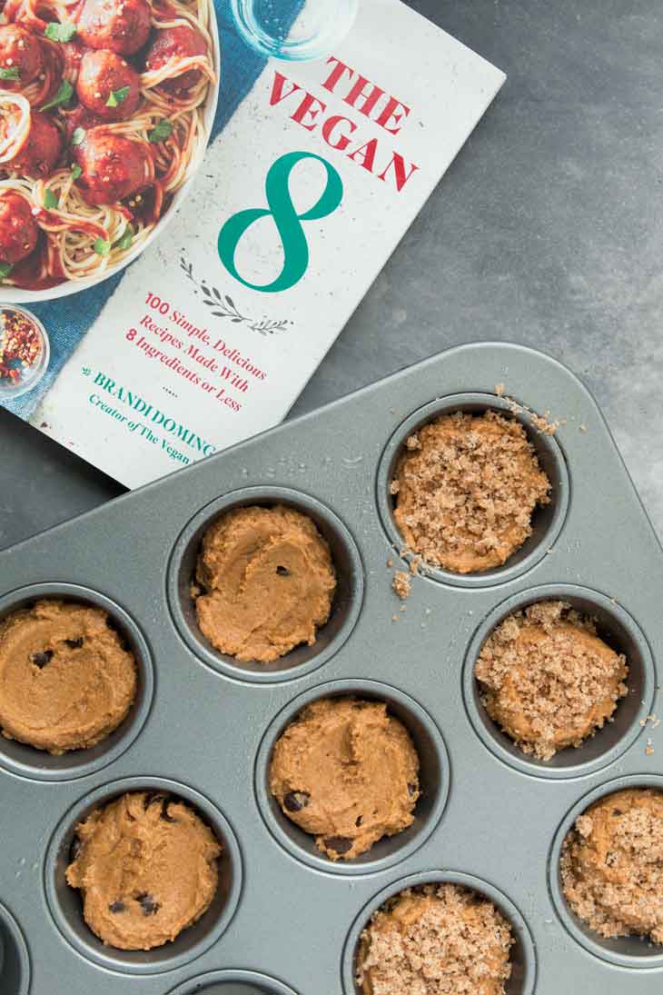 An overhead photograph of vegan pumpkin muffin batter filled in the pan, with the vegan 8 cookbook off to the side.