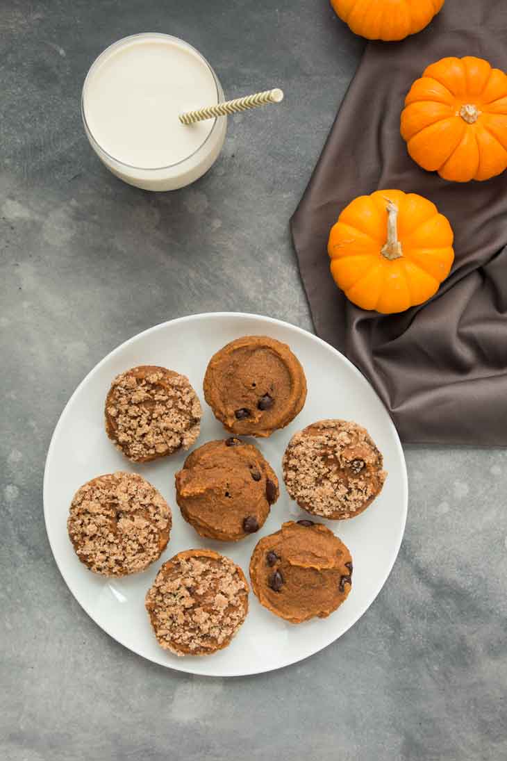 An overhead photograph of a plate of vegan pumpkin muffins with a glass of vegan milk and mini pumpkins off to the side.