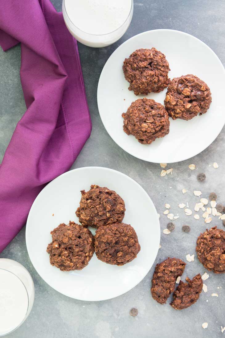 Overhead photograph of two serving plates of chocolate breakfast cookies. There are two glasses of milk and some broken cookies off to the side.