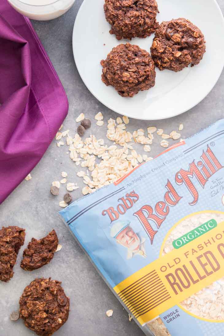 Overhead photograph of chocolate breakfast cookies on a plate with bob's red mill oats bag off to the side along with some chocolate chips.