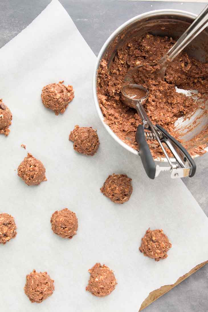 Overhead photograph of chocolate breakfast cookie batter being scooped out and placed on a baking sheet.