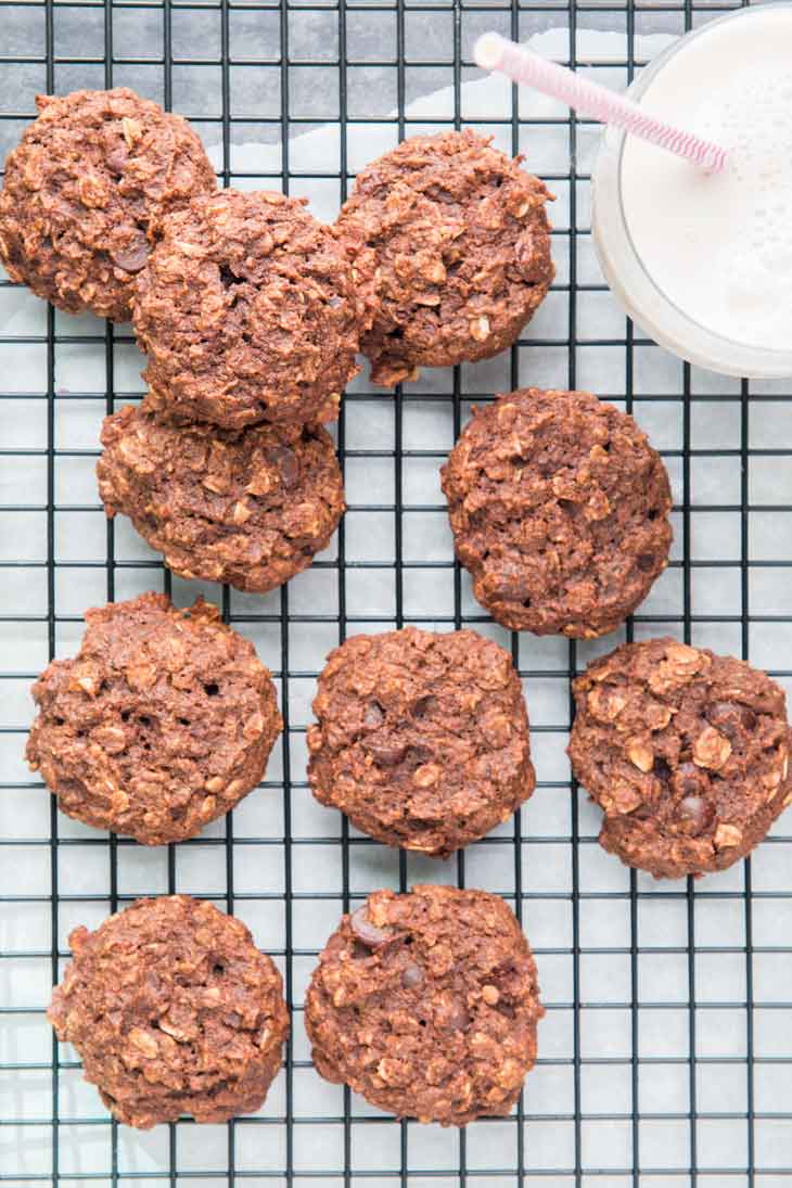 Overhead photograph of chocolate breakfast cookies cooling on a black cooling rack with a glass of milk off to the side.