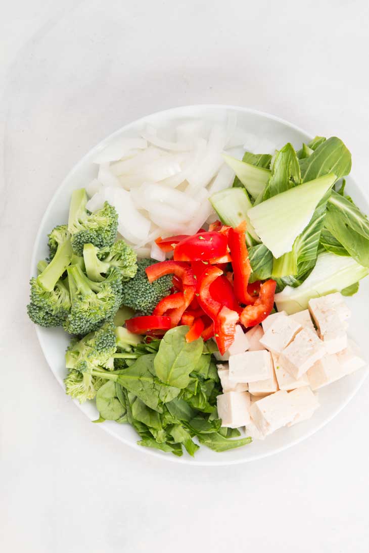 Overhead photograph of veggies in a white bowl being used for a healthy stir fry recipe. 