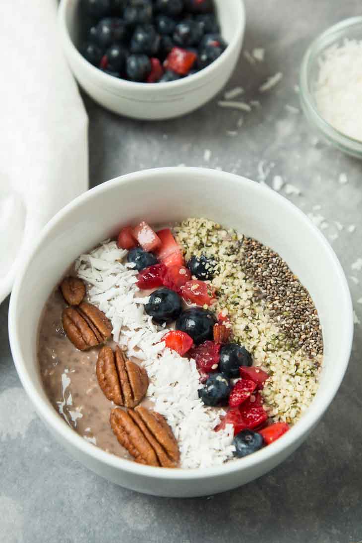 A 45 degree photograph of a vegan keto breakfast bowl. There's some shredded coconut and mixed berries in the background. 