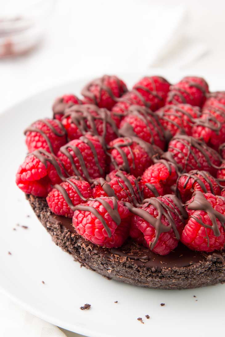 A side close up of vegan chocolate pie topped with raspberries and drizzled with chocolate.