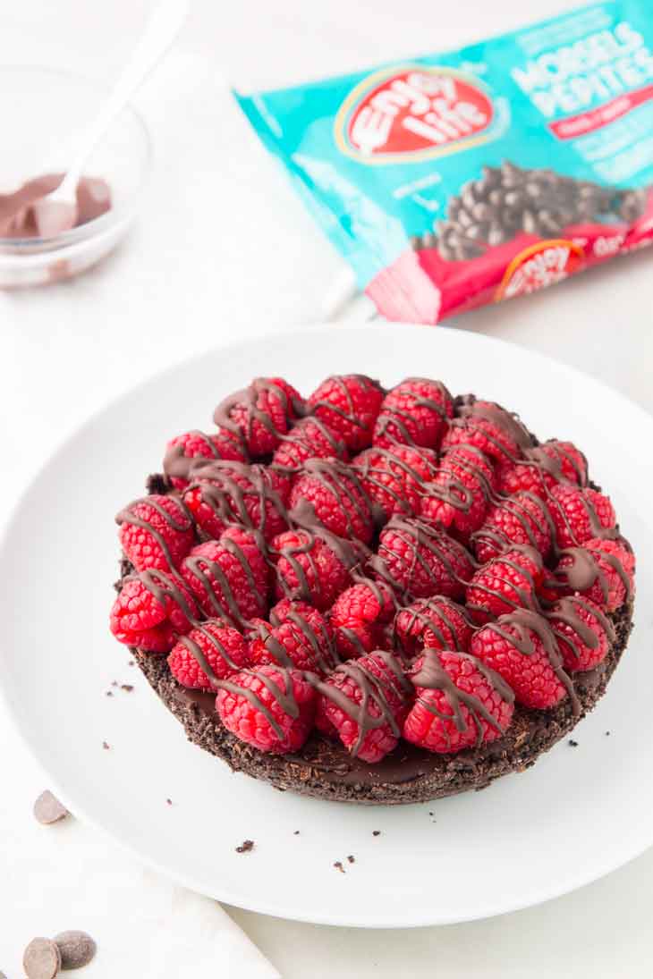 A side photograph of the entire vegan chocolate pie sitting on a white plate, with a bag of enjoy life foods chocolate chips in the background.