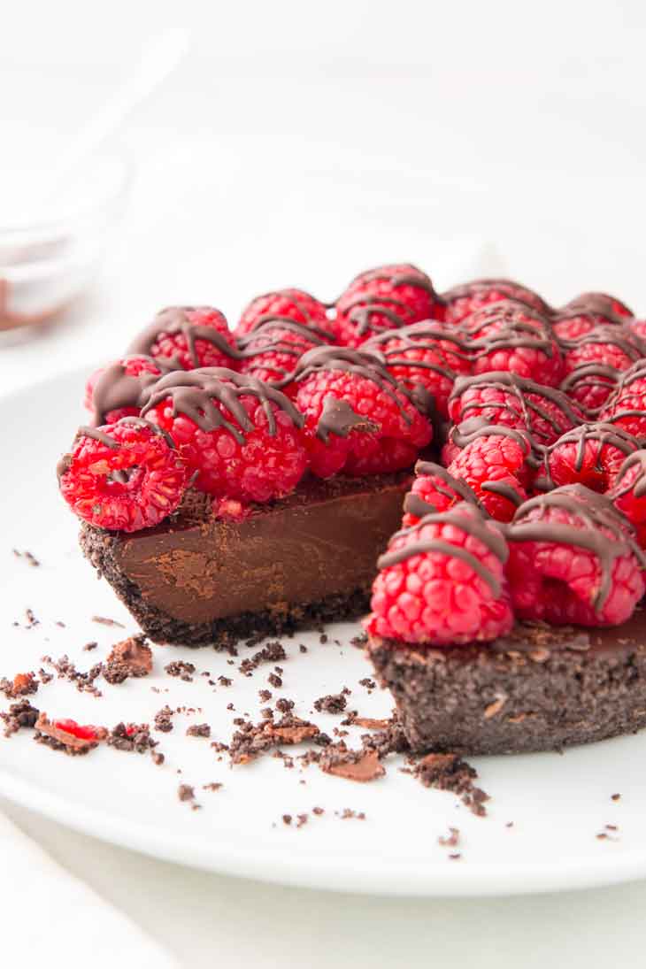 A side photograph of vegan chocolate pie with raspberries on top and drizzled with chocolate.