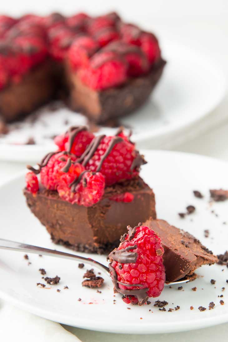 A bite taken out of a piece of vegan chocolate pie, topped with raspberries.