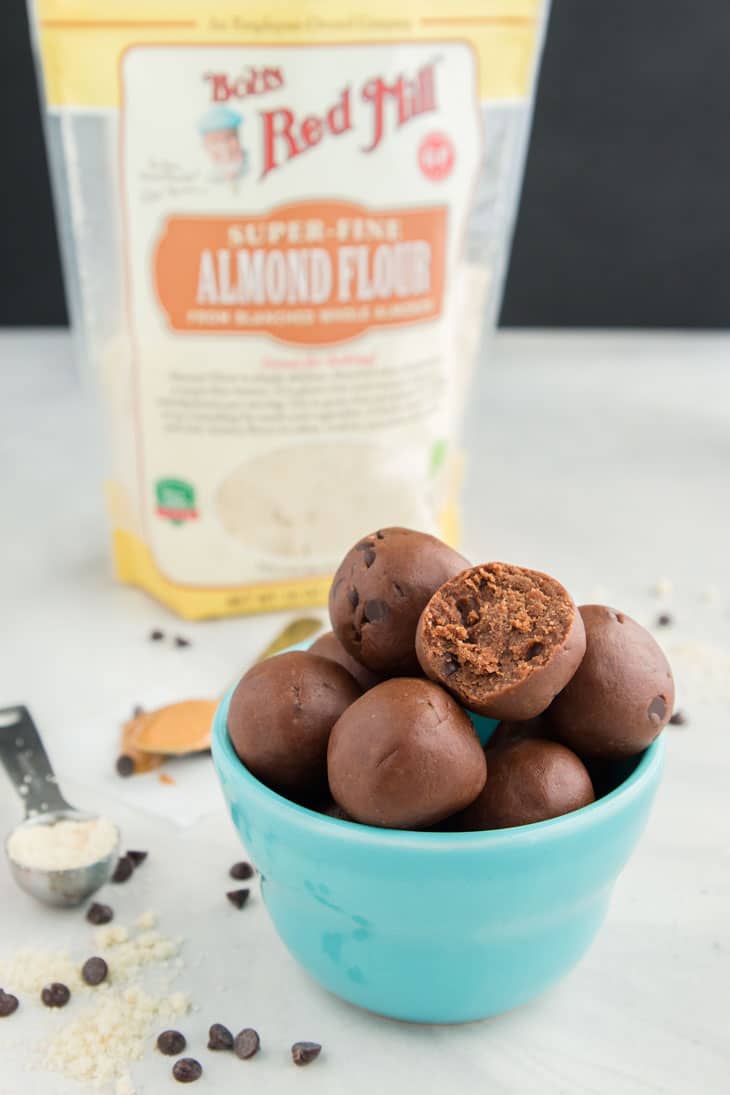 Chocolate cookie dough bites in a blue bowl with a bag of bob's red mill almond flour in the background. 